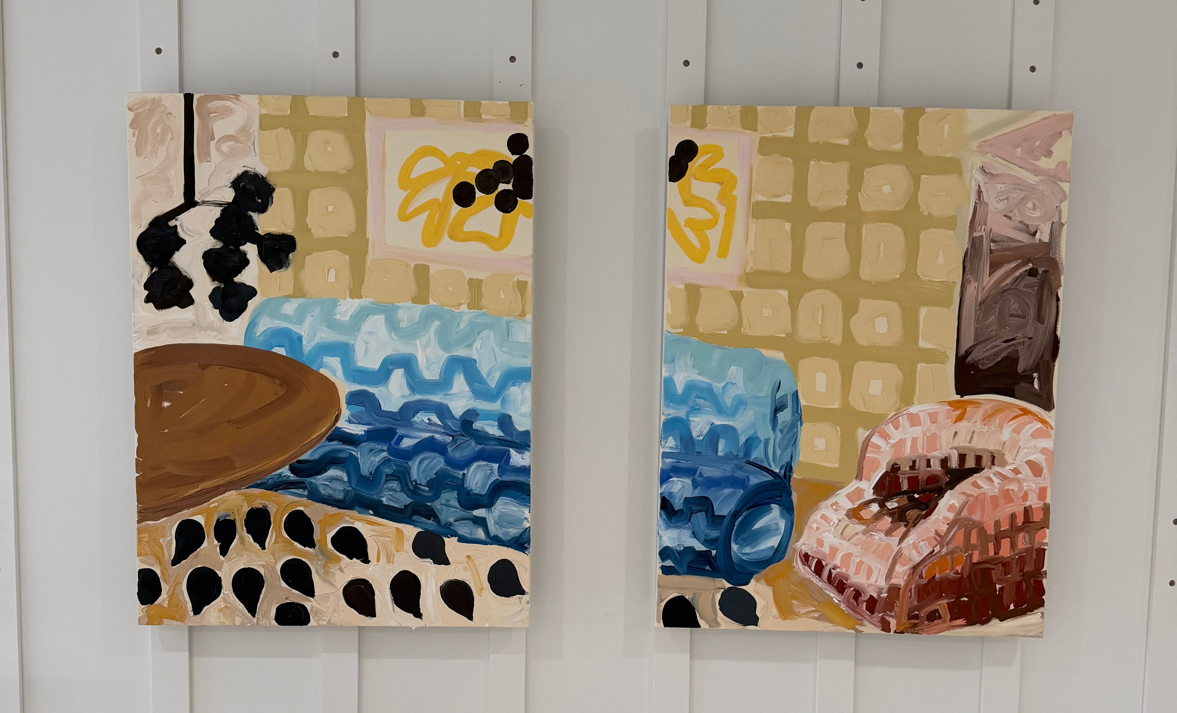 Two abstract art prints on a white wall with a wooden floor.